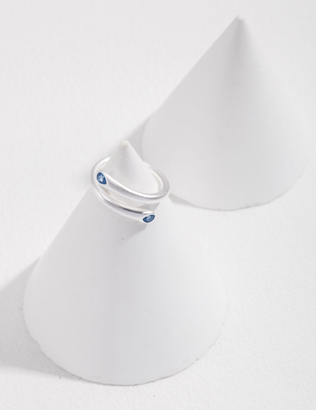 A minimalist silver wrap around ring showcasing a stunning aquamarine, displayed on a white cone.