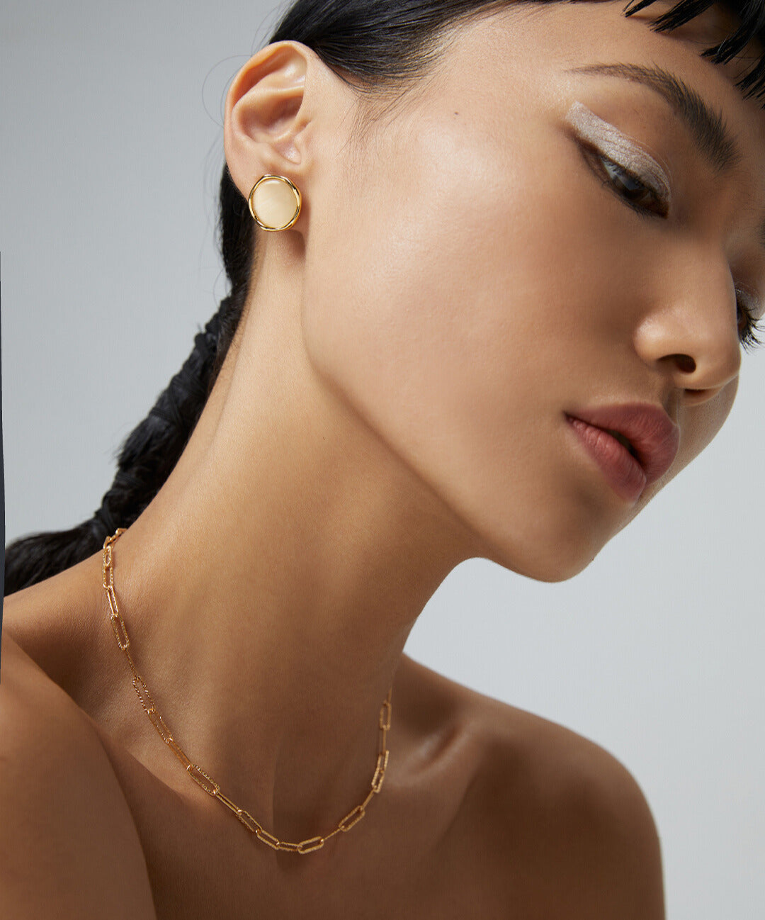 A woman wearing a gold chain necklace with champagne gold cat's eye studs.