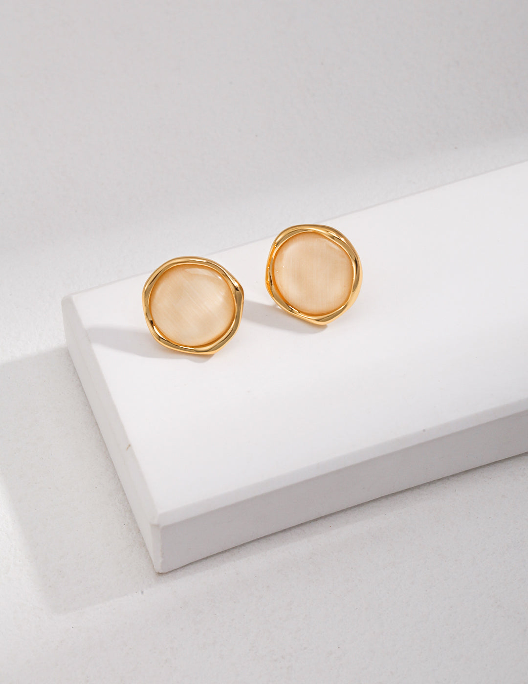 Shimmering gold studs with cat's eye gemstones, placed on a pristine white background.