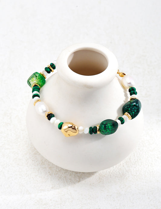 A white vase adorned with green and gold beads, featuring a bracelet made of Agate, Freshwater Pearls, Malachite, and Nacre.