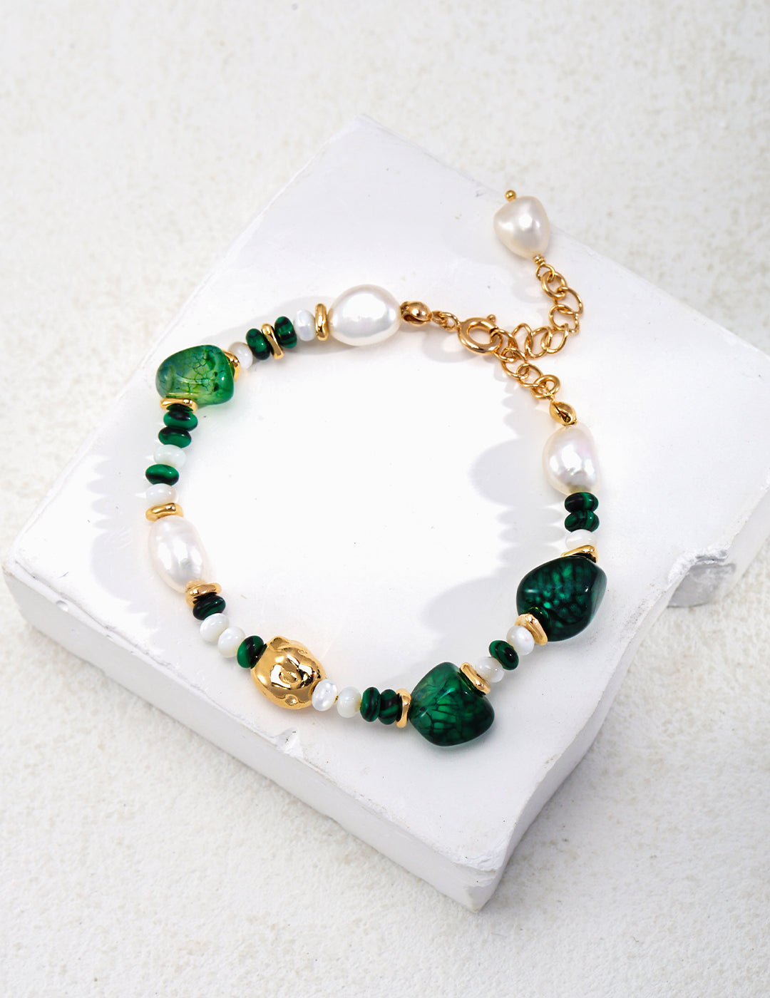 A stylish green and white bracelet adorned with gold and pearl charms made of Agate, Freshwater Pearls, Malachite, and Nacre.