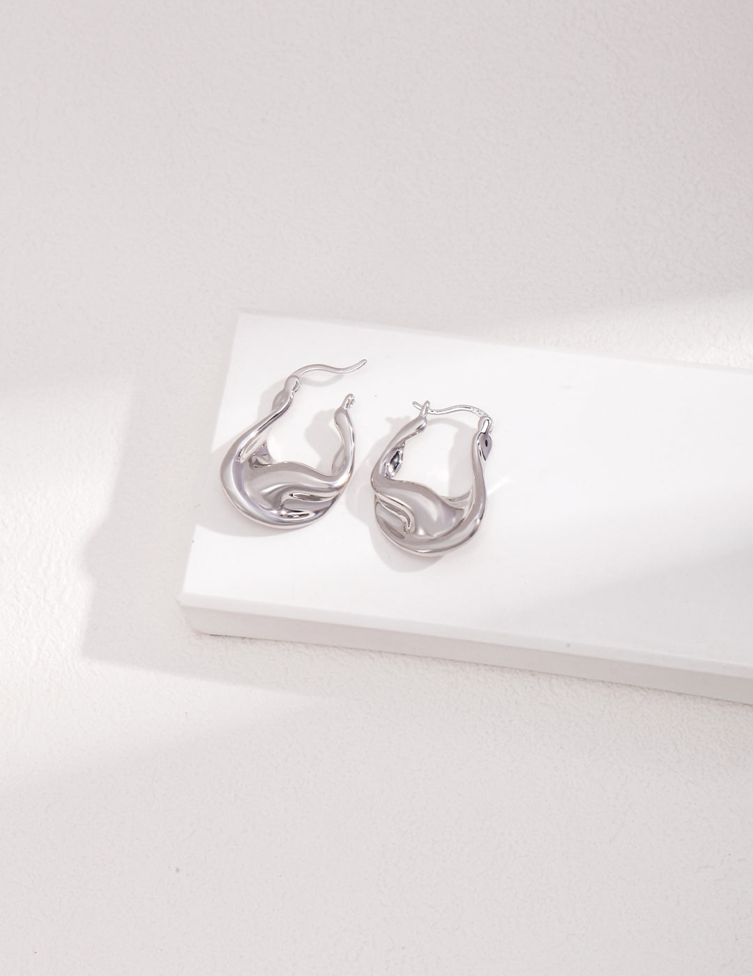 Shiny silver drop earrings on white background.