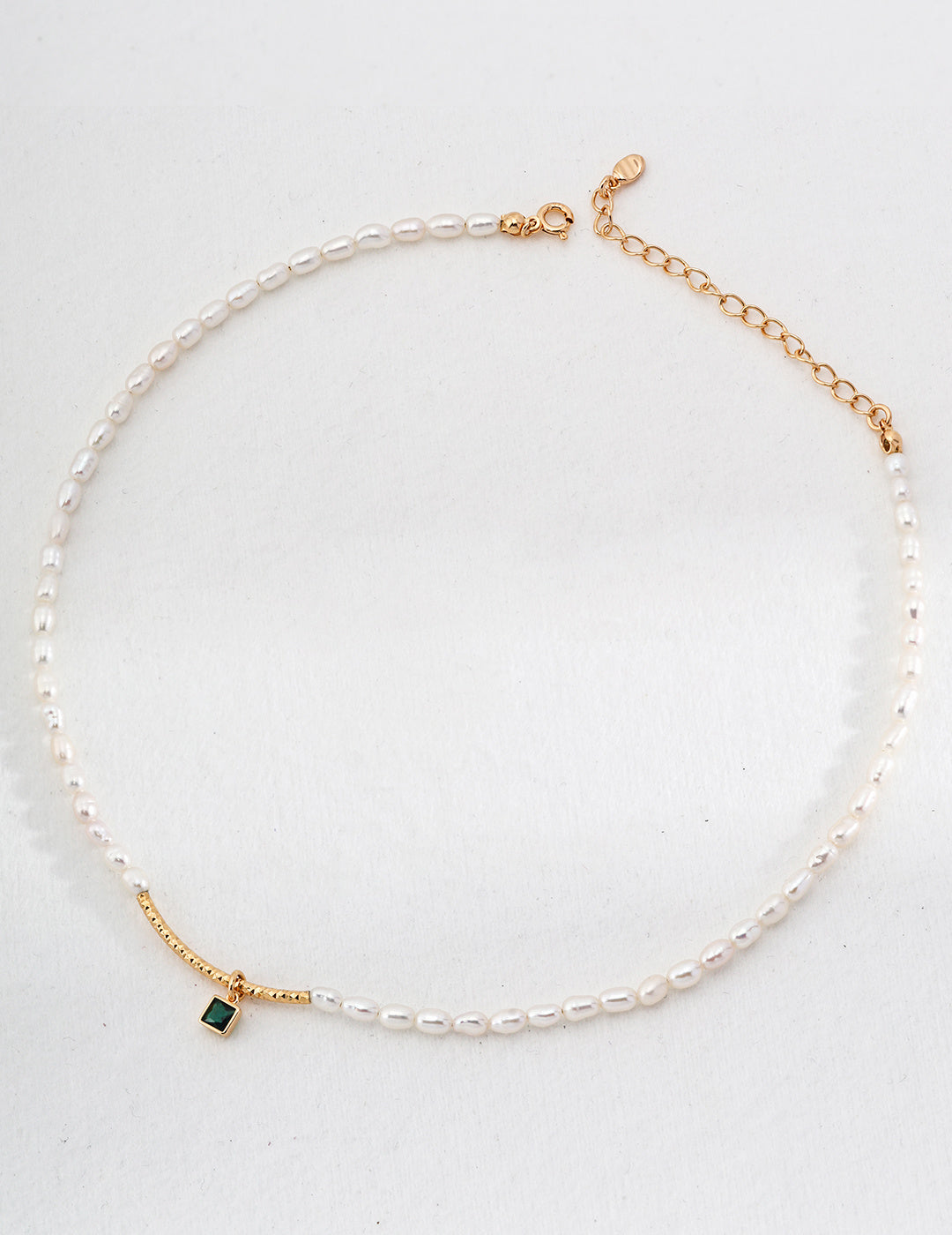 A stunning gold-plated necklace featuring a lustrous pearl and a vibrant green zirconia stone, perfect for any elegant occasion.