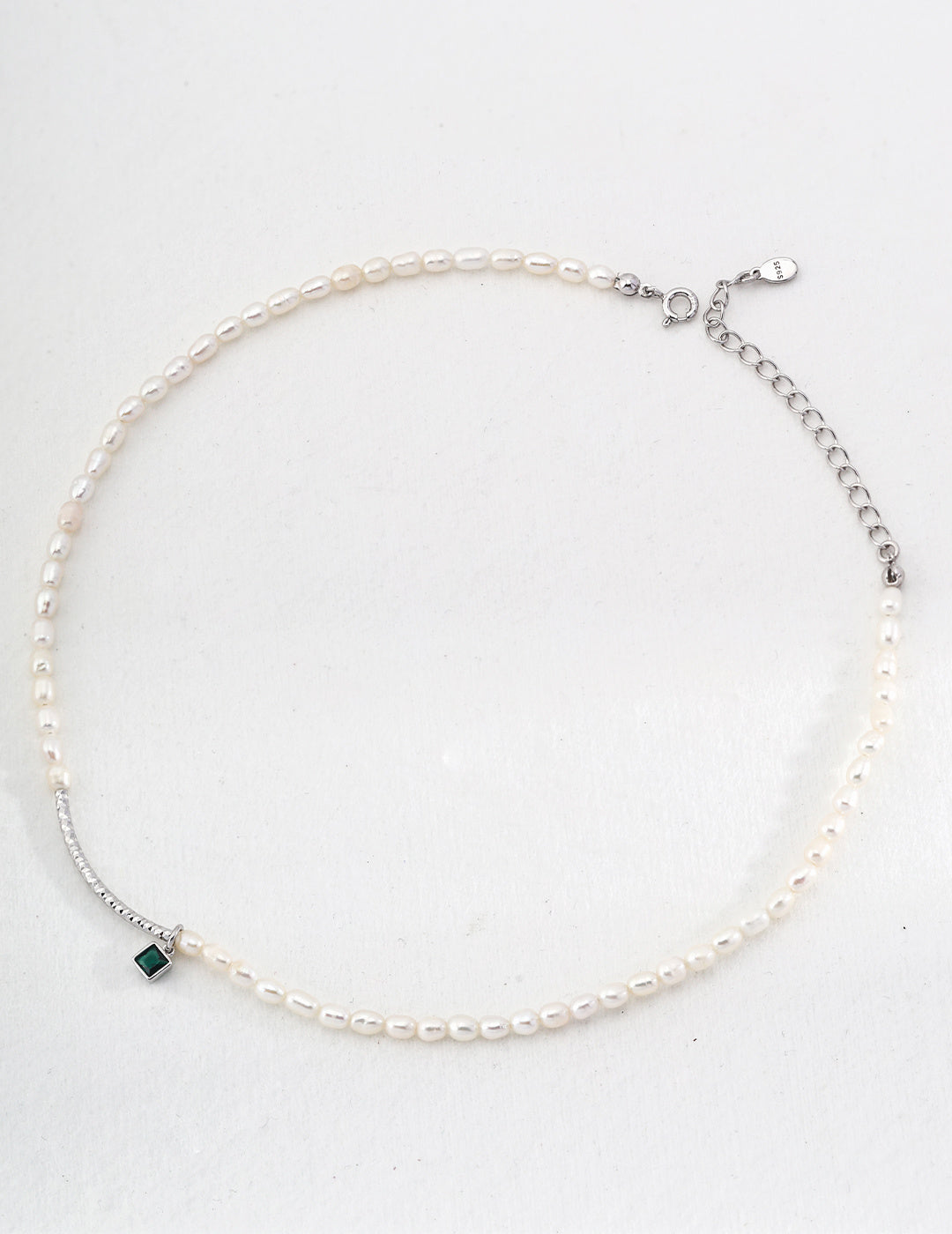 A beautiful white pearl necklace adorned with a vibrant green zirconia stone, showcasing timeless elegance and style.