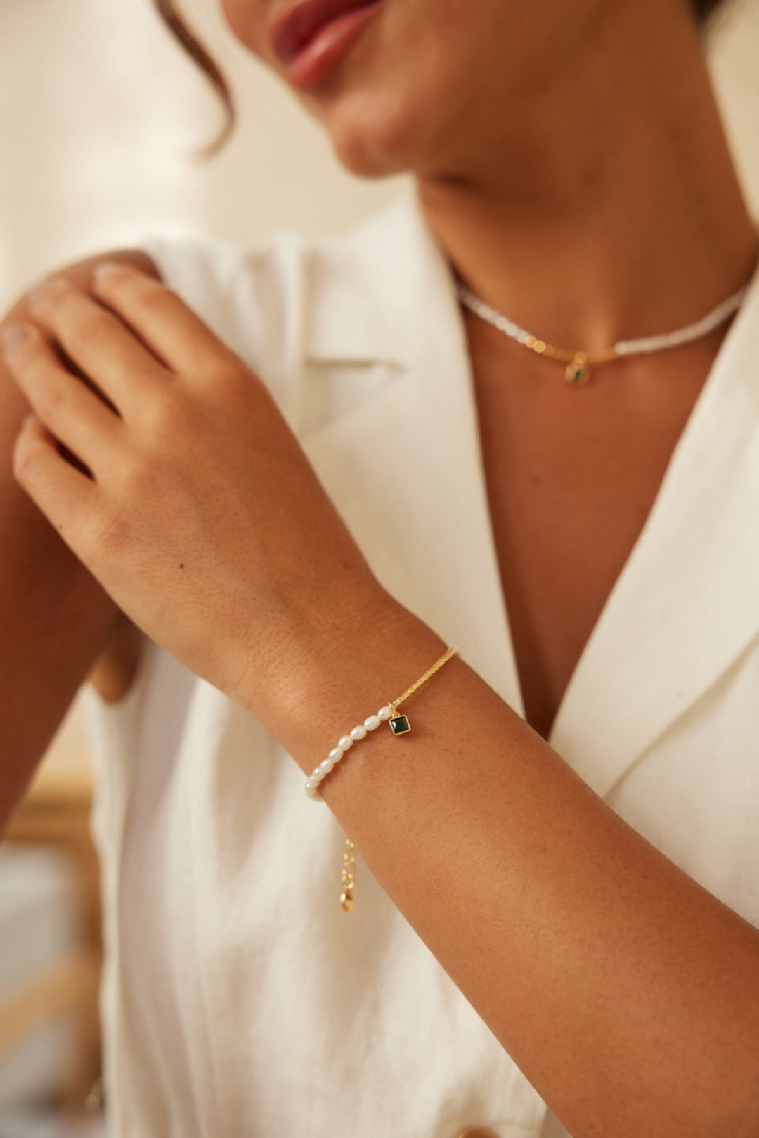 A woman dressed in a white shirt, showcasing a gold bracelet and a shimmering zirconia pearl bracelet.