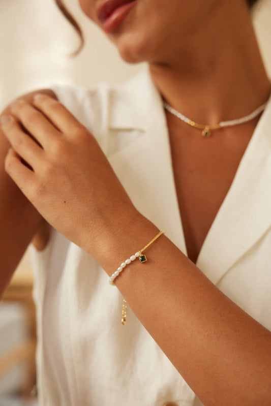 A woman dressed in a white shirt, showcasing a gold bracelet and a shimmering zirconia pearl bracelet.