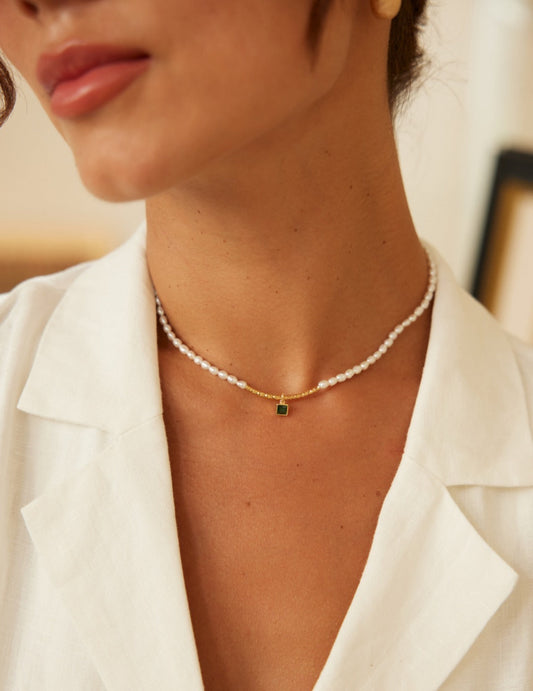  A woman in a white shirt wearing a necklace adorned with a green zirconia stone and freshwater pearls.