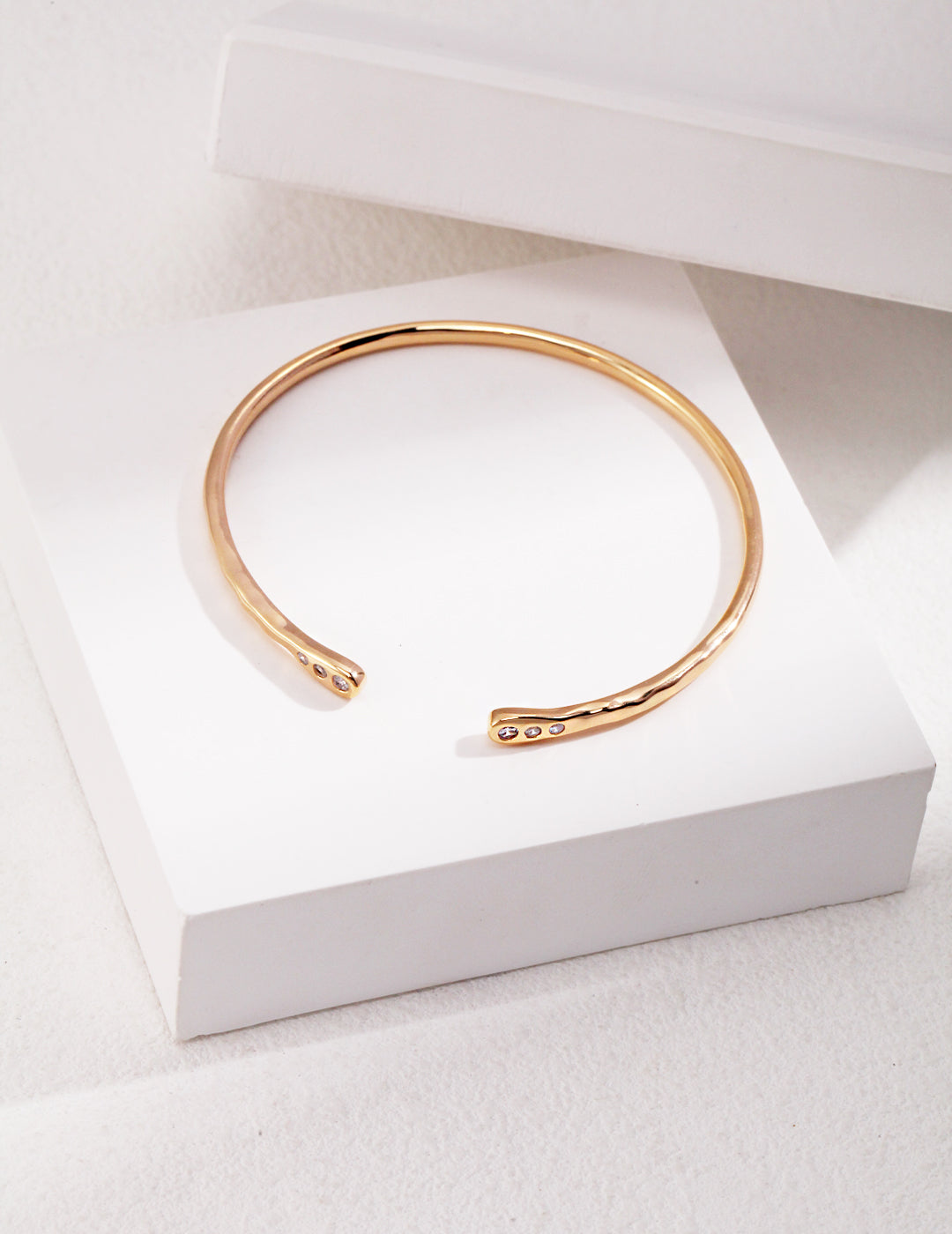 Dainty gold bangle bracelet adorned with cubic zirconia on white box.