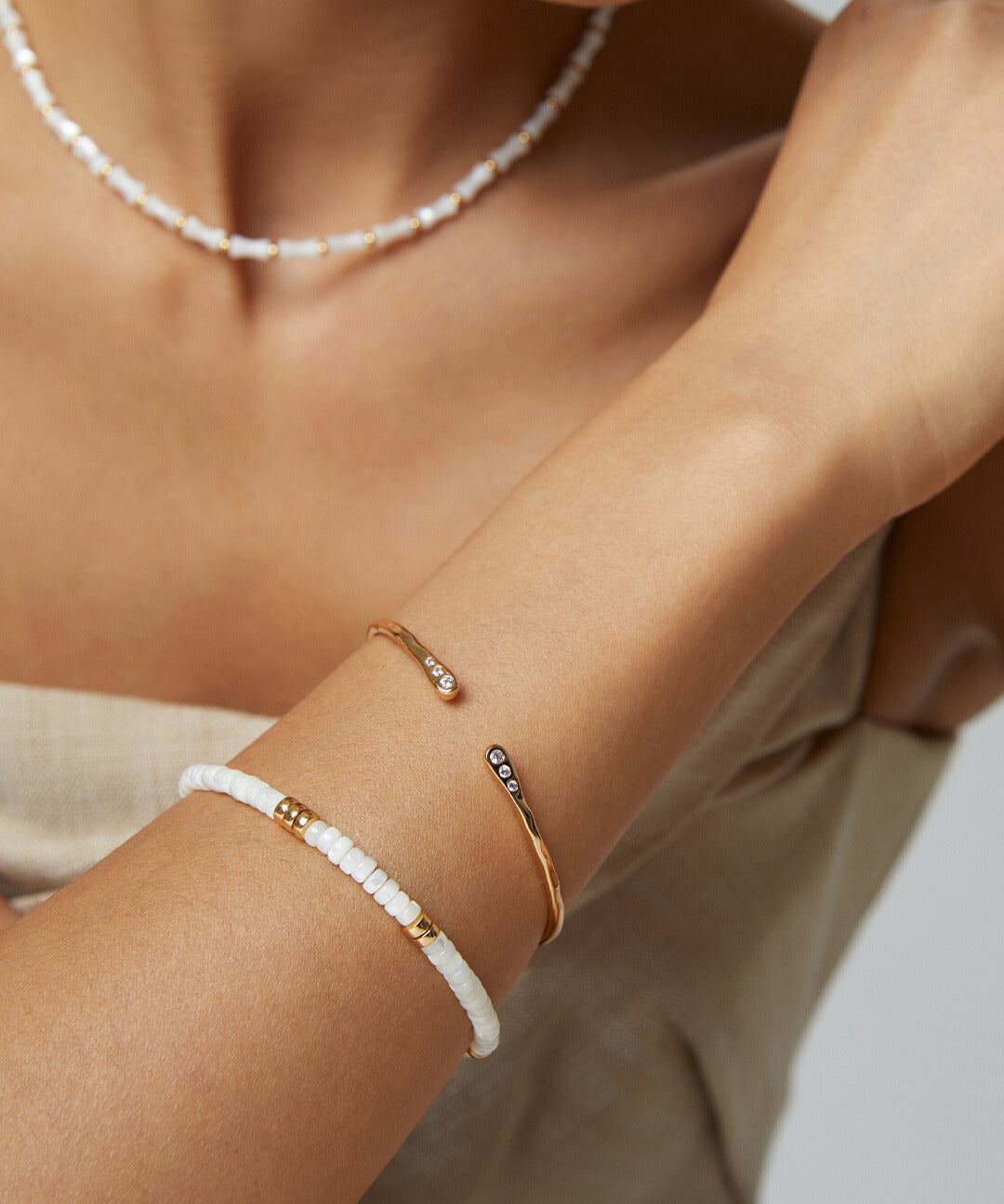 Woman wearing a white and gold bracelet, featuring gold bangle with dainty cubic zirconia.