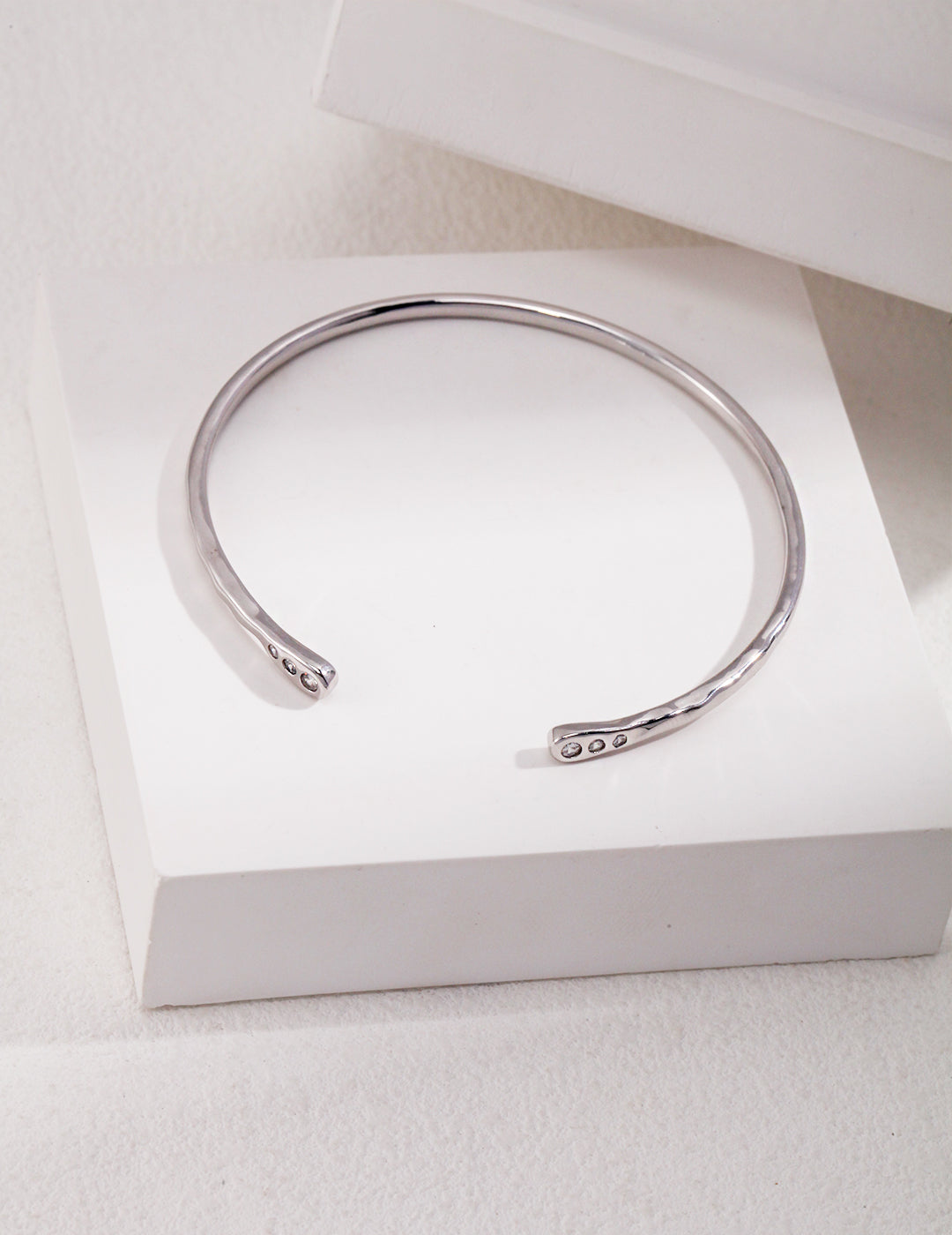 A silver bangle bracelet with delicate cubic zirconia, resting on a white box.