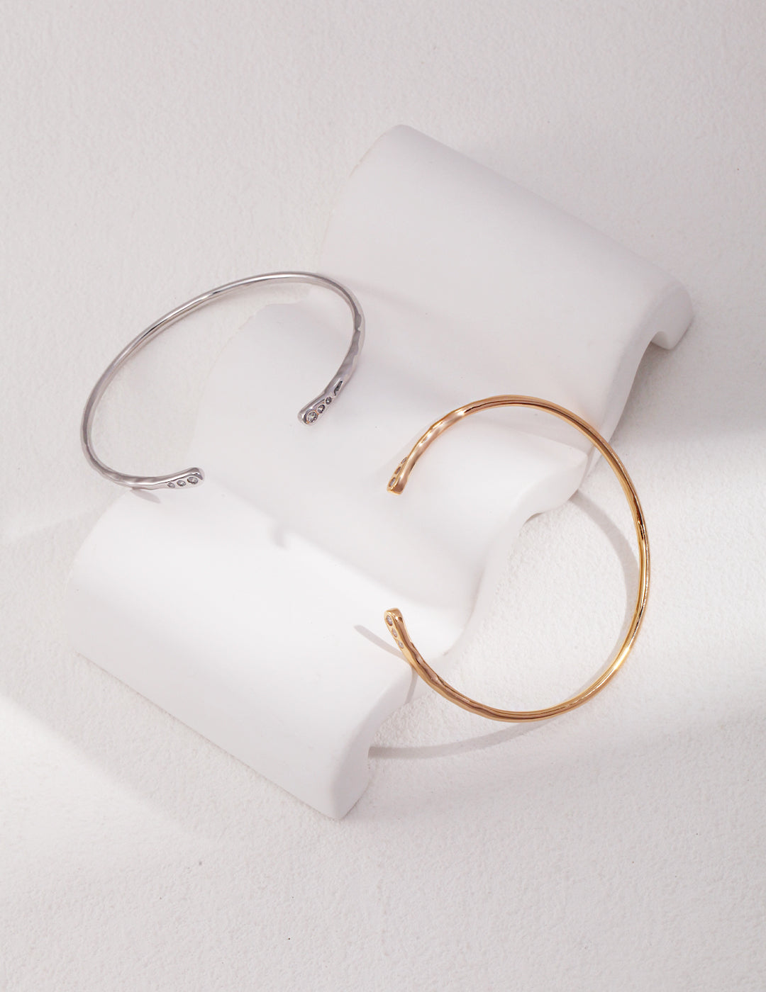 Two elegant bangles, one gold and one silver, adorned with delicate cubic zirconia, resting on a white surface.