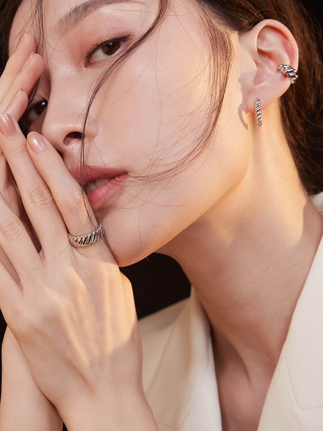  Elegant woman wearing silver twisted hoops and matching jewelry, with a ring on her finger, looking contemplative.