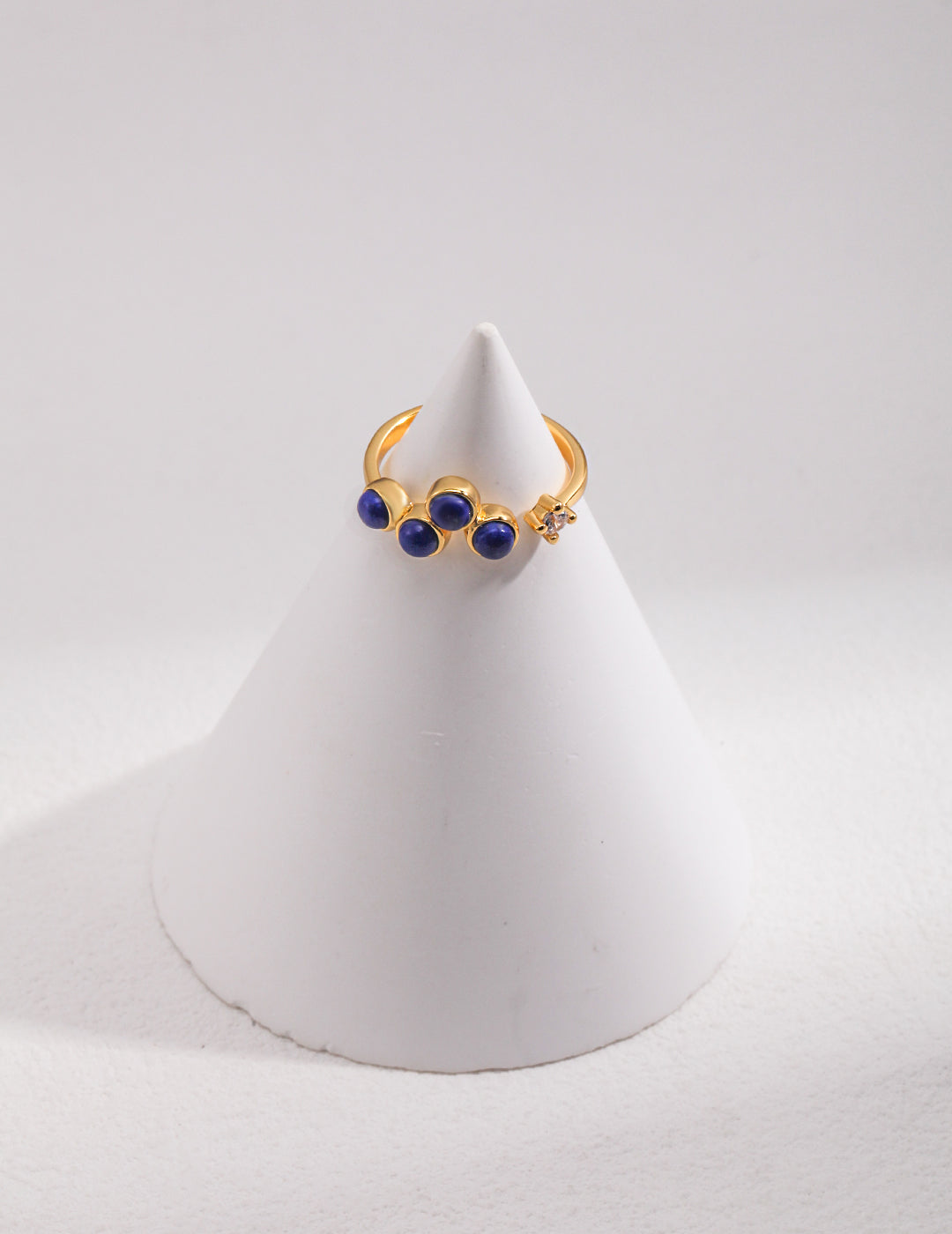 Gold plated open ring with lapis lazuli and cubic zirconia stones on top of a white cone.