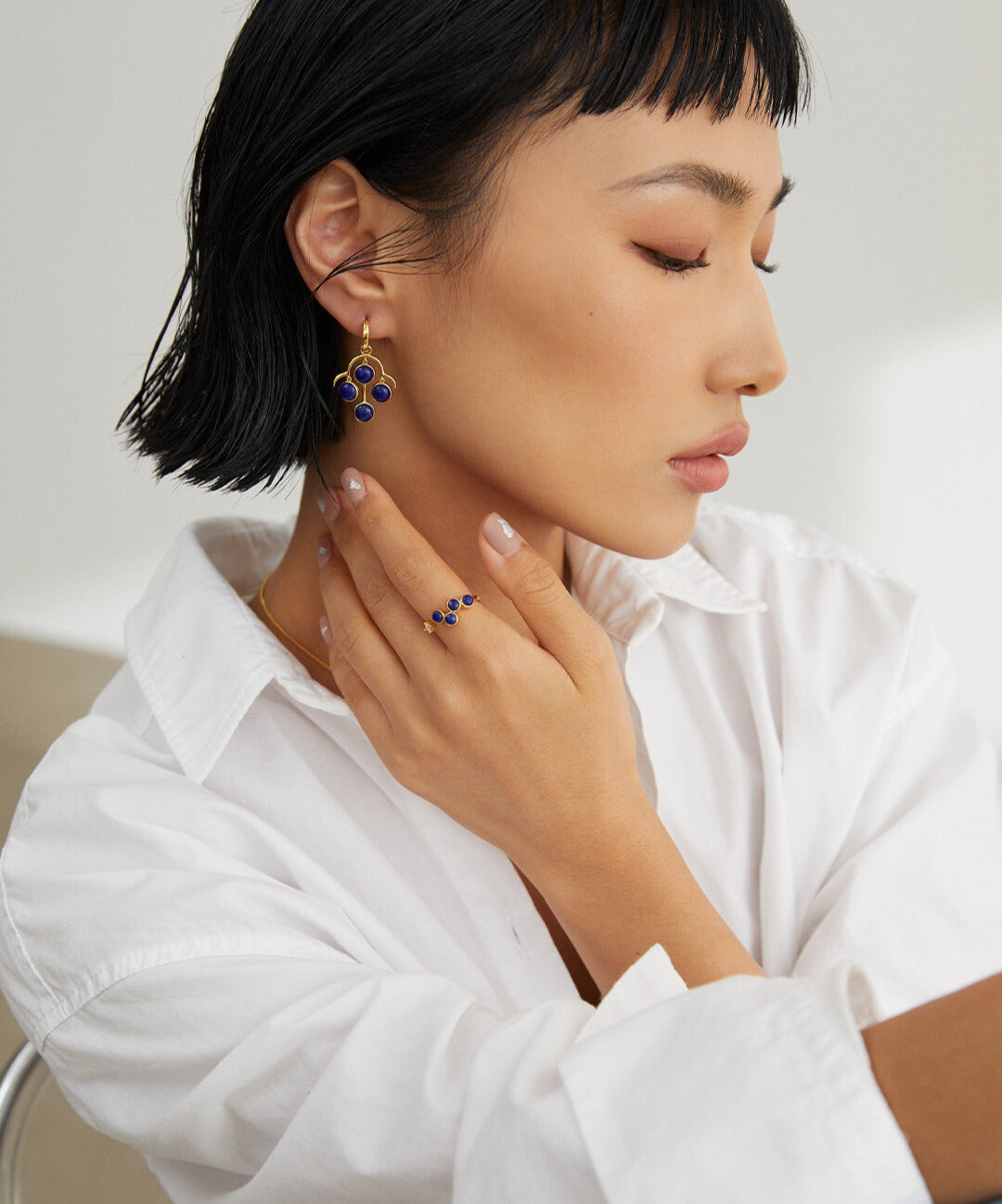 Lady wearing white shirt, blue earrings, gold plated ring with lapis lazuli & cubic zirconia.