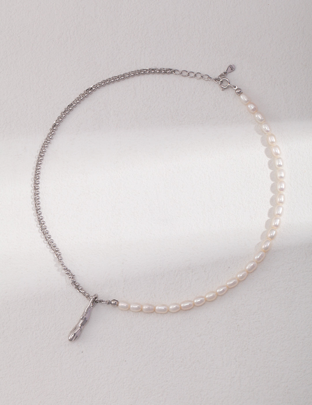 A silver necklace with a double layer chain and rice pearls, creating an elegant pearl necklace.