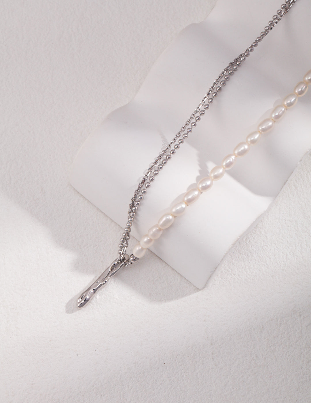 A silver necklace with a cross pendant and rice pearls on a half double layer chain.