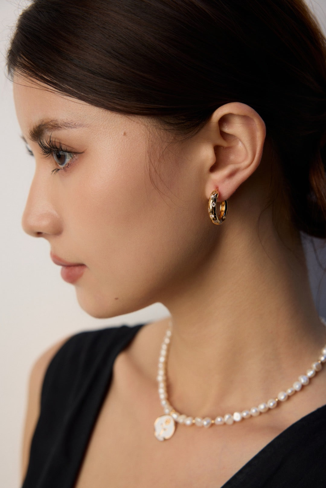 Side profile lifestyle view of a model wearing the thick gold Jocelyn starburst hoop earring, illustrating how the textured metalwork catches light to create dynamic visual interest.