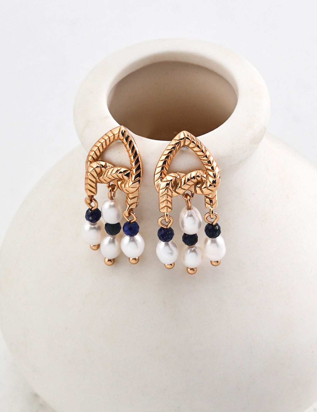 Stylish gold plated knot earrings featuring white pearls, and lapis lazuli.