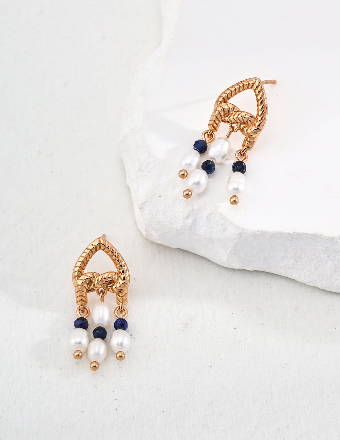 Elegant gold and blue earrings with pearls and lapis lazuli on white stone.