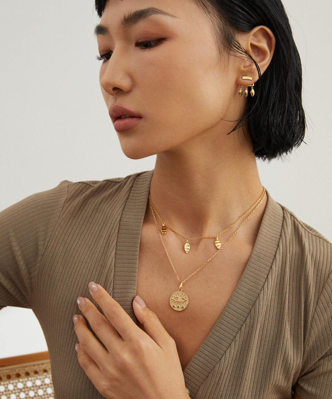 A woman wearing a gold necklace and earrings, featuring a gold plated chain with triple leaf pendants.