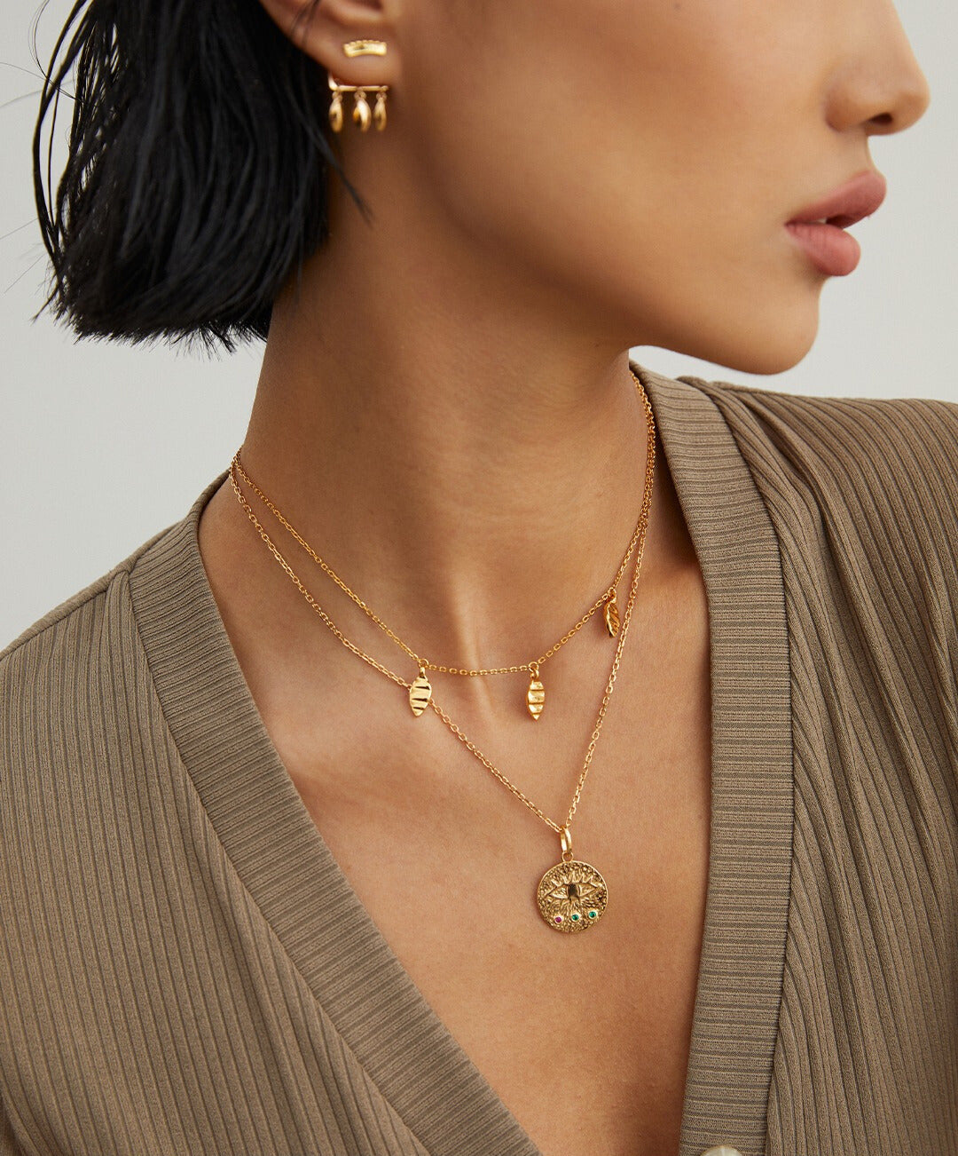 Model in gold chain necklace with coin charm, triple leaf pendants.