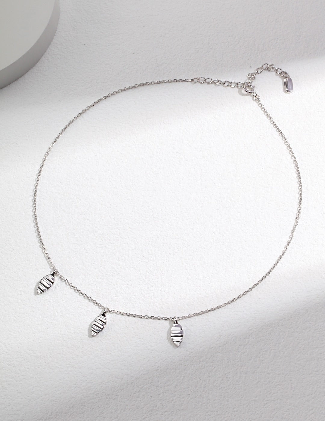 A silver chain necklace with three leaf pendants hanging from it.