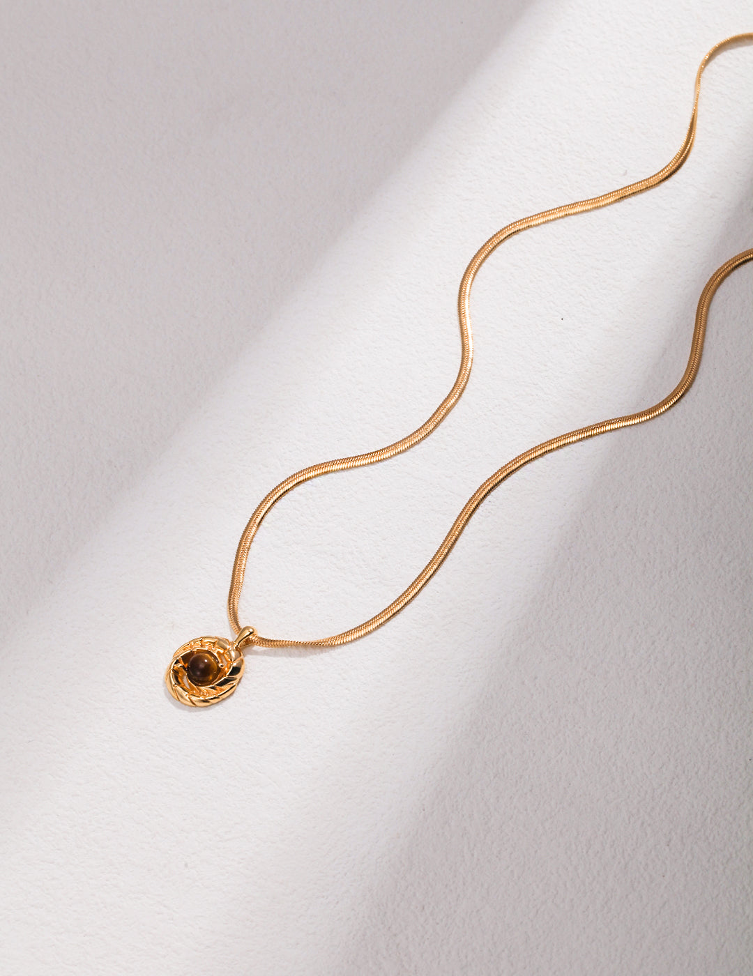 A gold necklace with a small disc, featuring Tiger's eye.