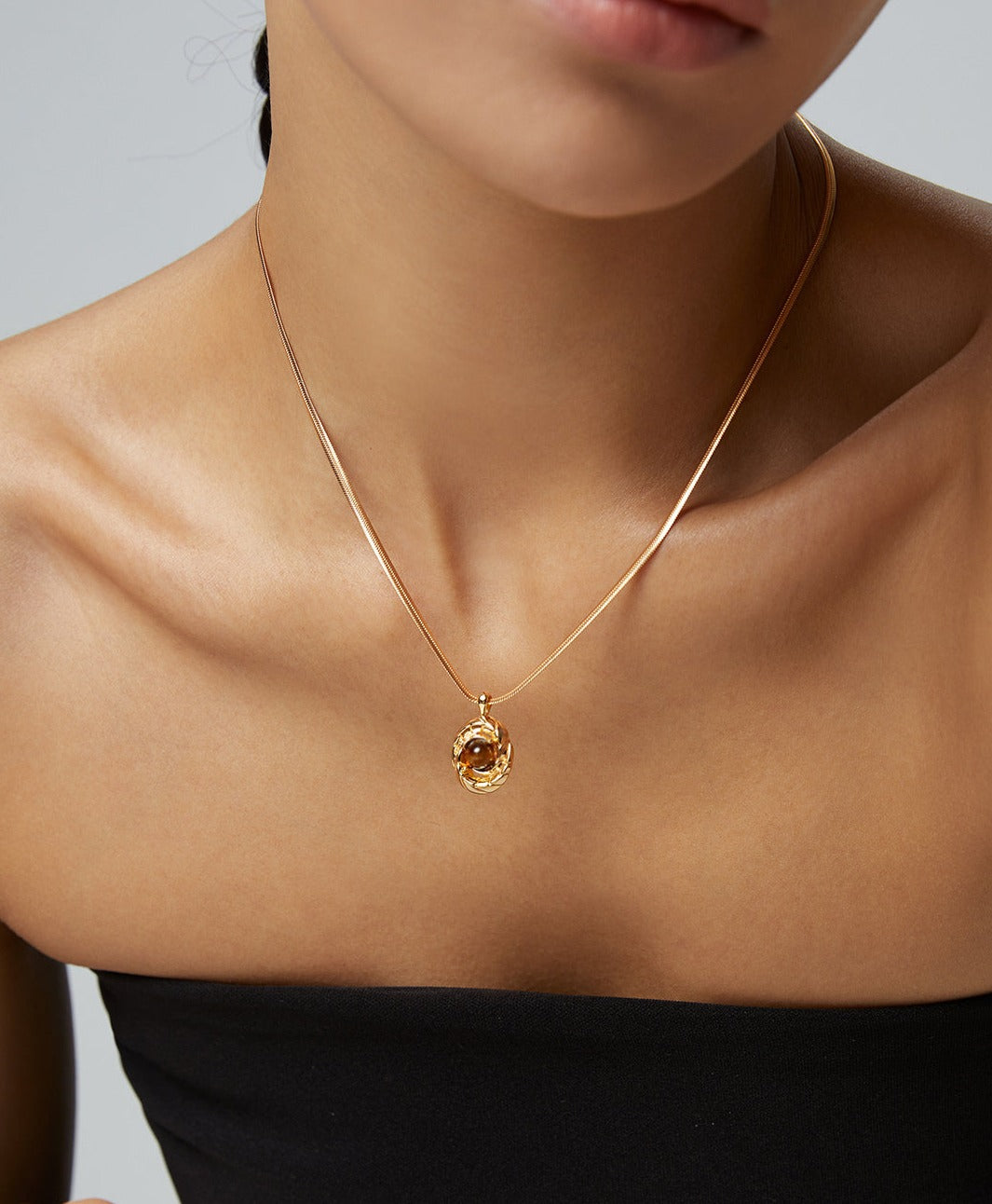 A woman wearing a necklace with a gold pendant made of tiger's eye, a captivating and elegant accessory.