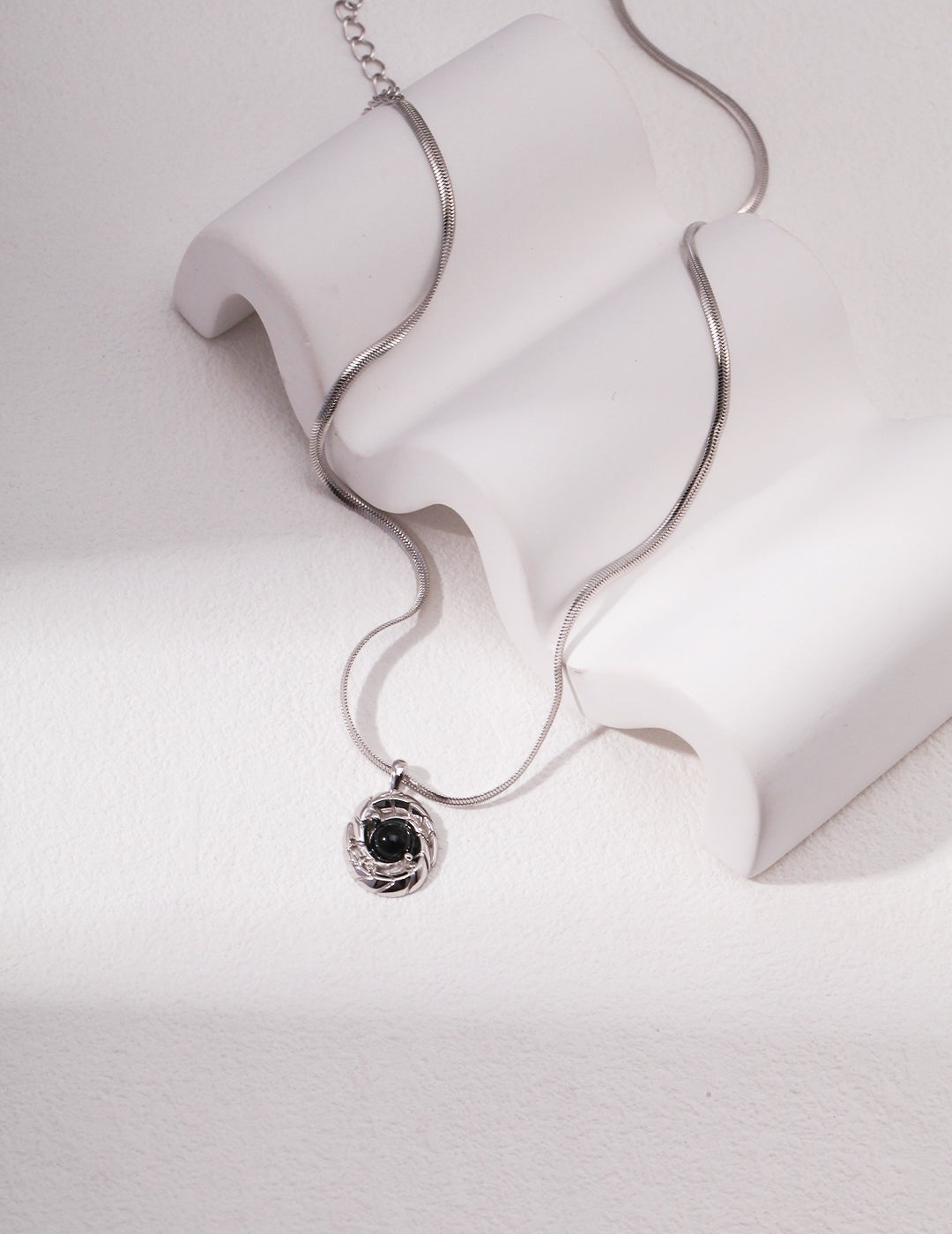 Silver black agate stone necklace on white surface.