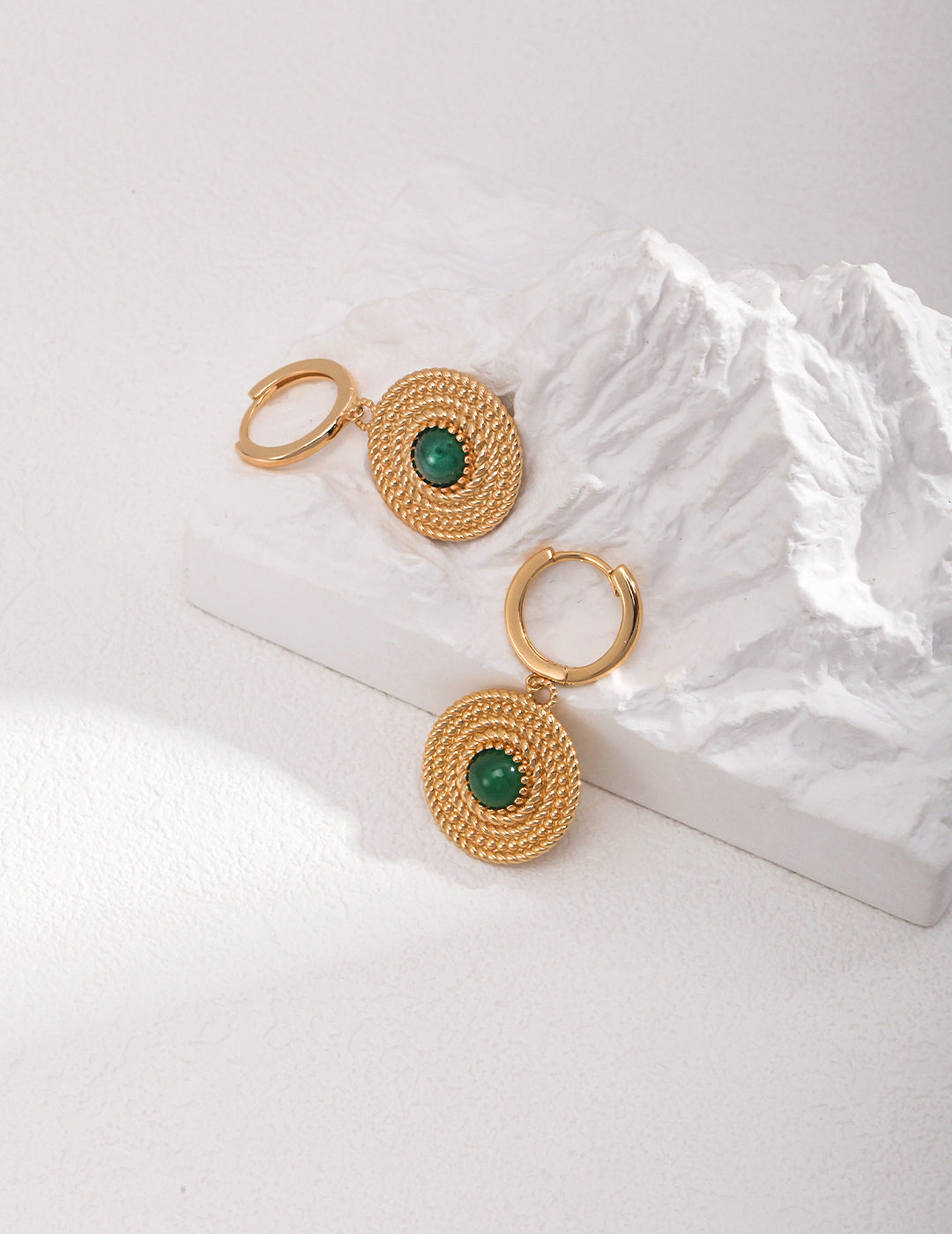 Gold plated hoop earrings with green chalcedony stones, placed on mountain peak.