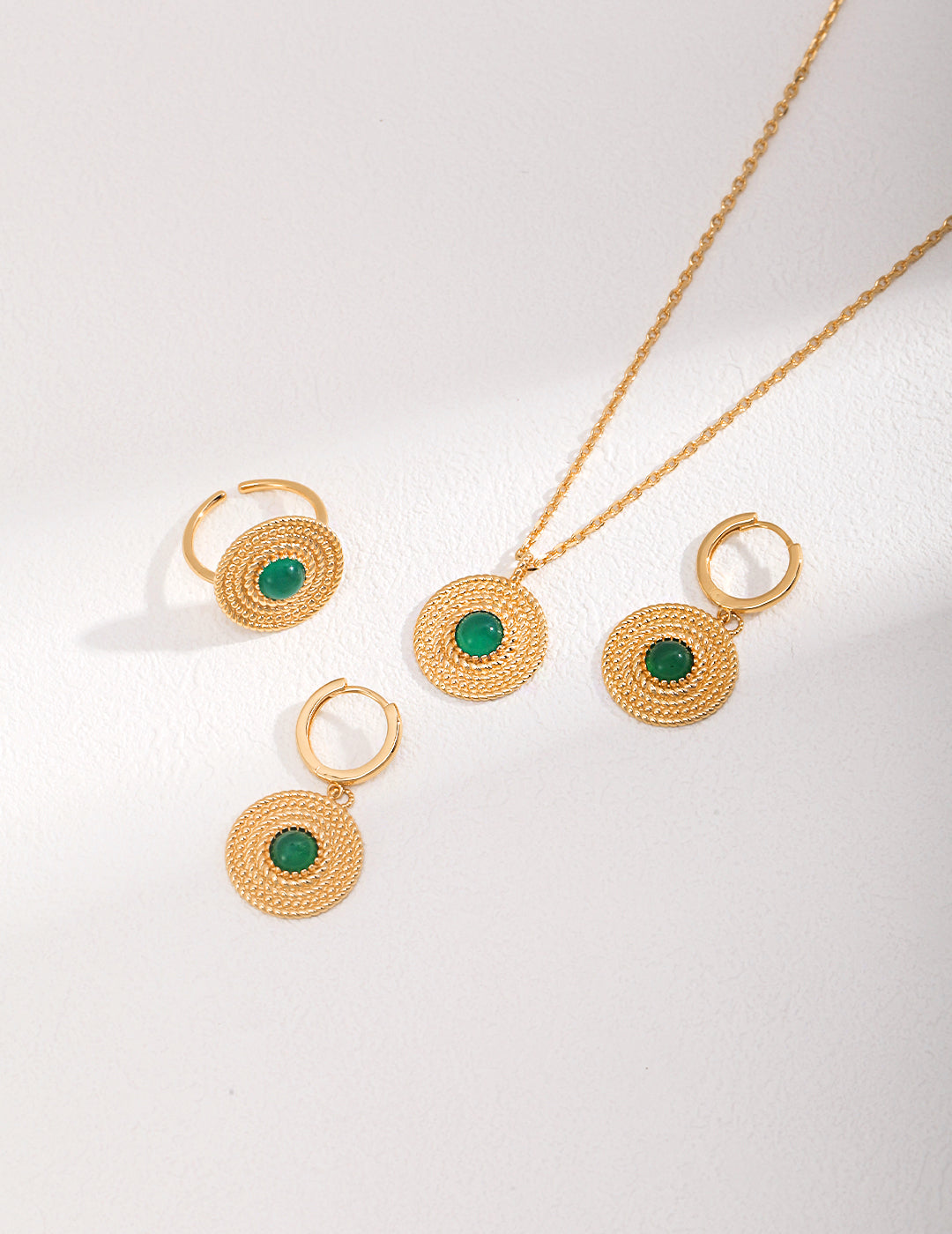 A stunning gold jewelry set with green stones, including a necklace with a chalcedony pendant and matching earrings and ring.