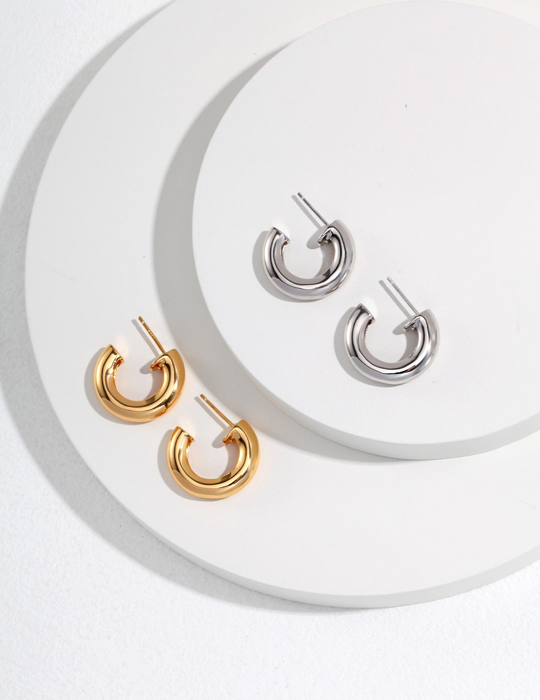 Two pairs of gold and silver hoop earrings neatly arranged on a white background.