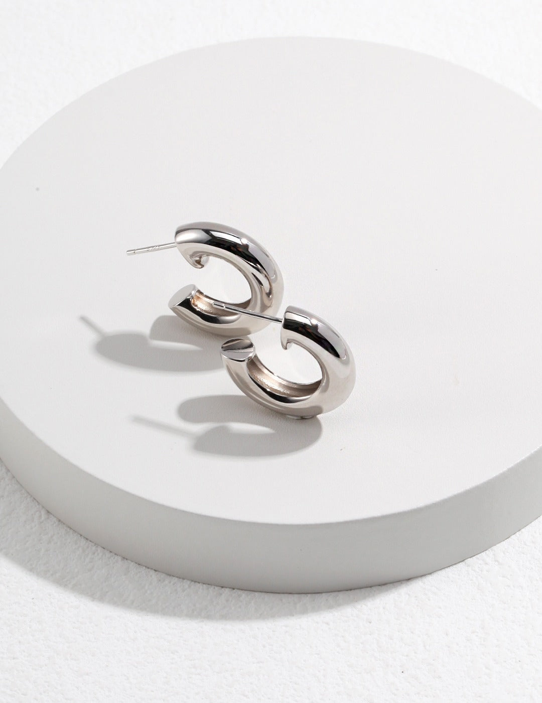 A pair of silver hoop earrings resting on a white surface, adding elegance and style to any outfit.