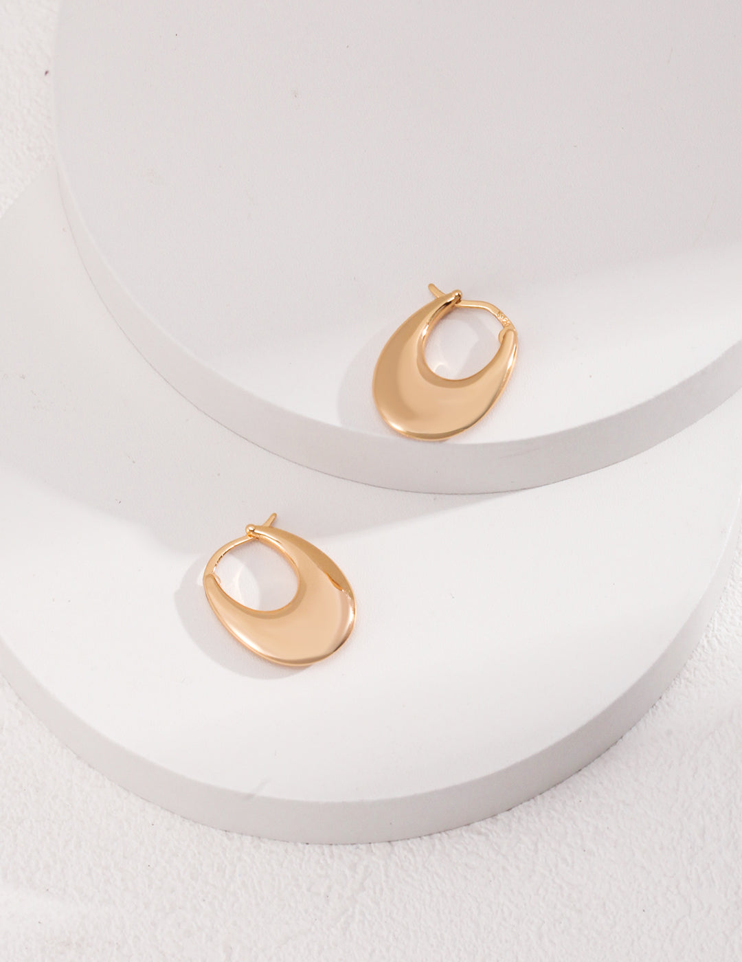 A pair of shiny gold hoop earrings on white surface.