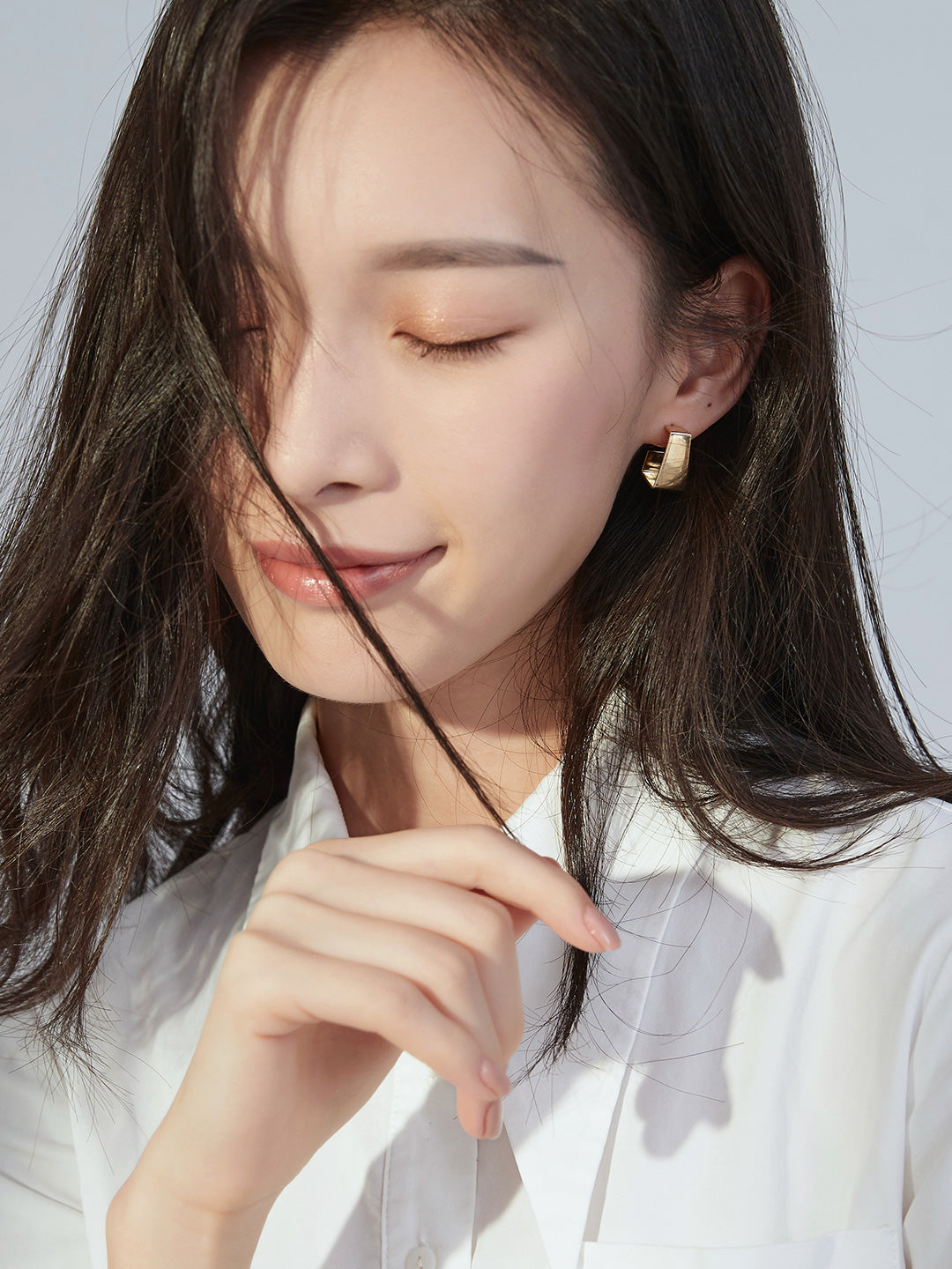 Long-haired woman in a white shirt, styled with gold chunky earrings.