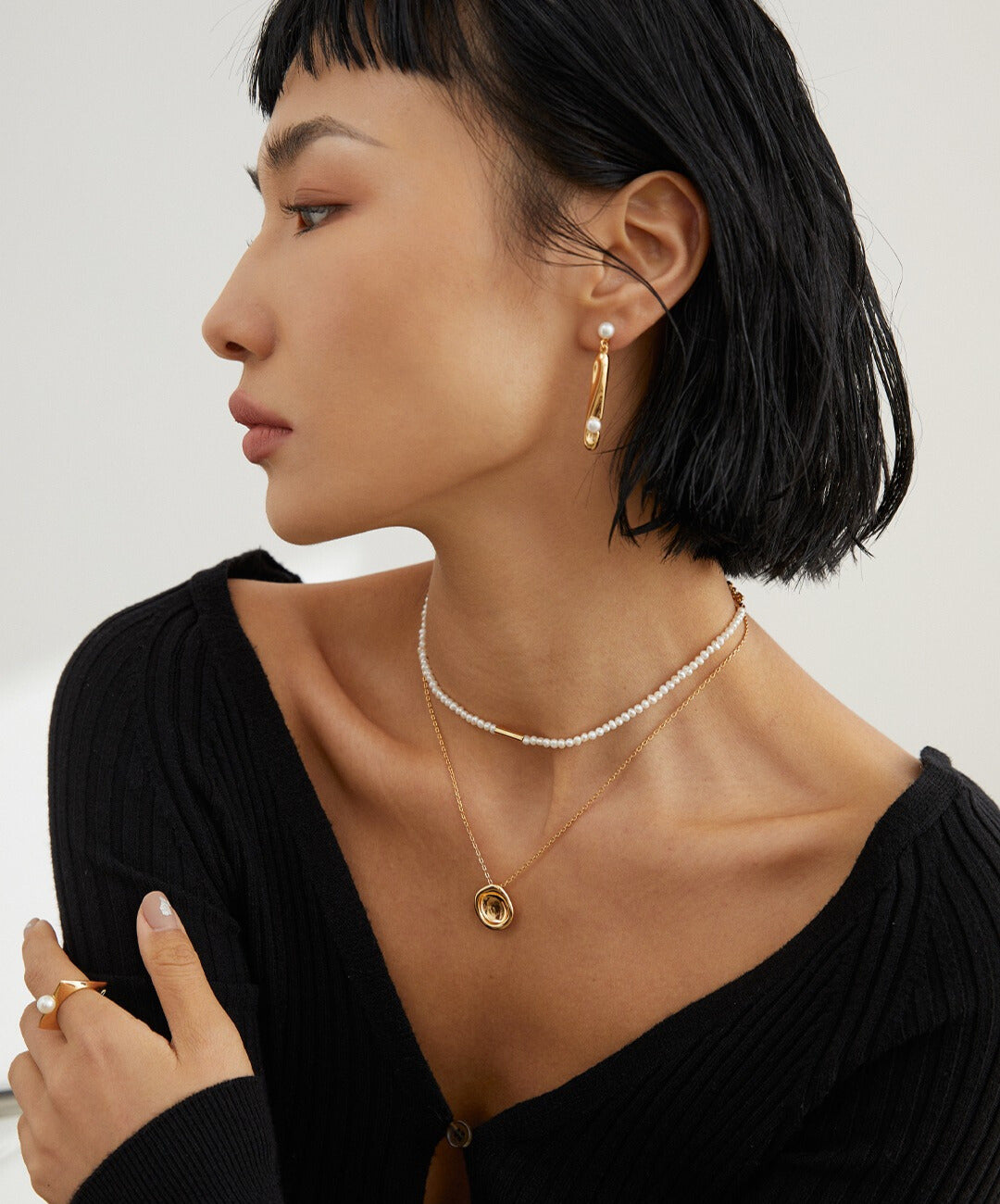 A stylish woman wearing a black sweater and a shimmering gold necklace, showcasing her fashion sense.