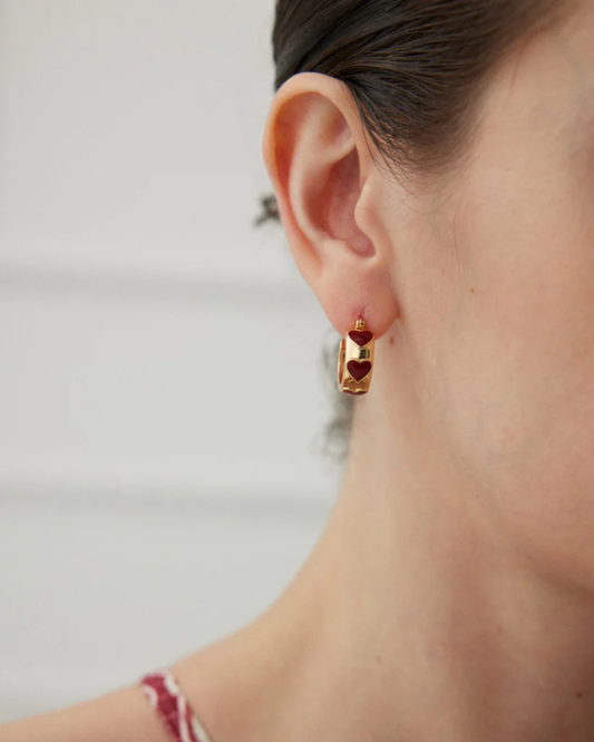 A woman displays heart-shaped hoop earrings in gold tone, enhancing her outfit with a trendy accessory.