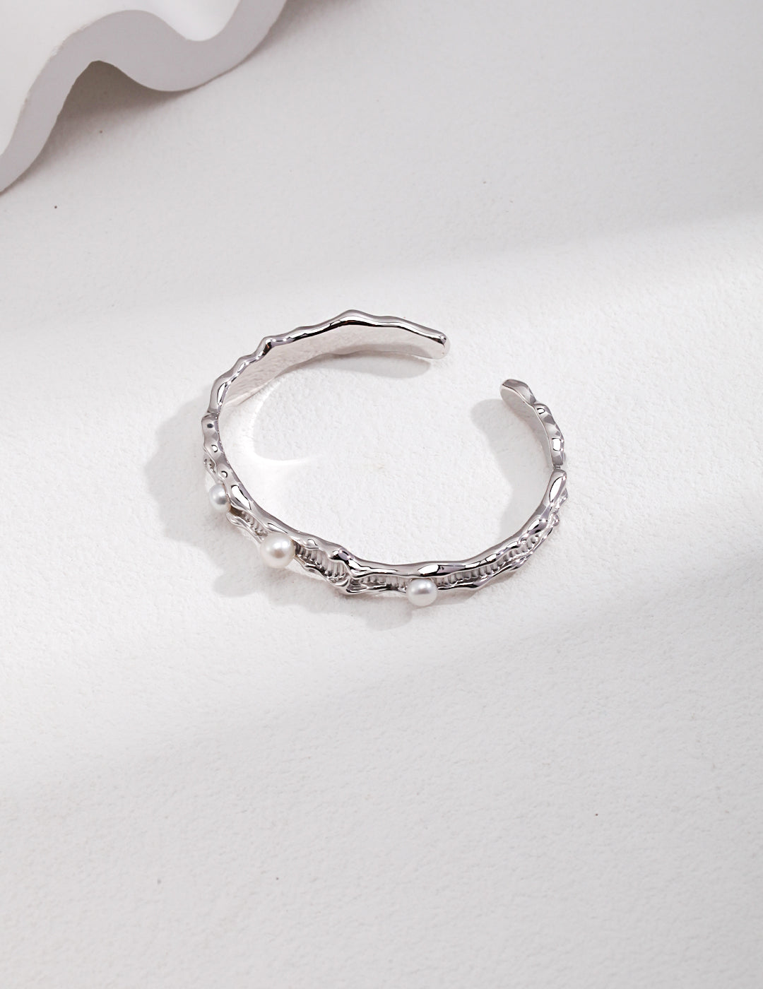 Silver bangle with wavy design, adorned with freshwater pearls.