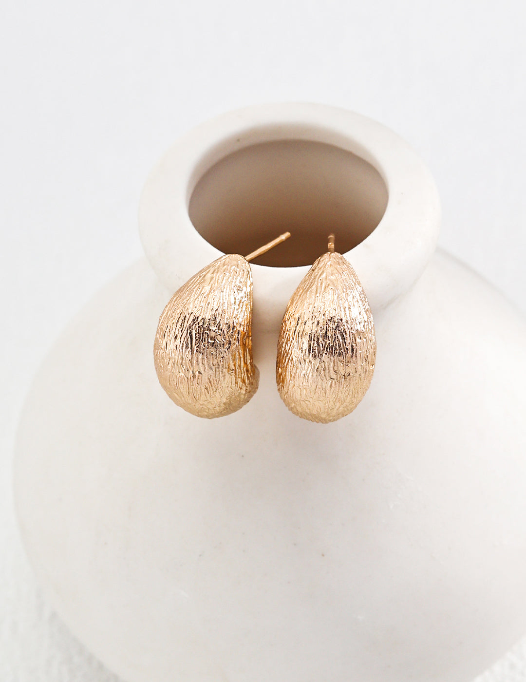 White vase holding gold plated tear drop earrings.