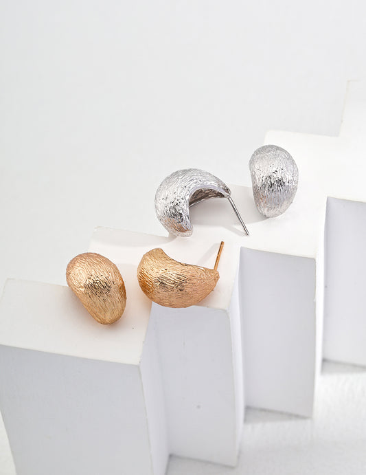 Textured tear drop earrings in silver and gold displayed on white surface.