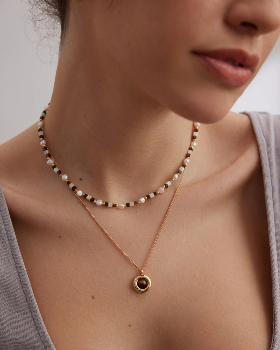 A woman displays a beautiful gold necklace with a pearl and a unique tiger's eye accent.