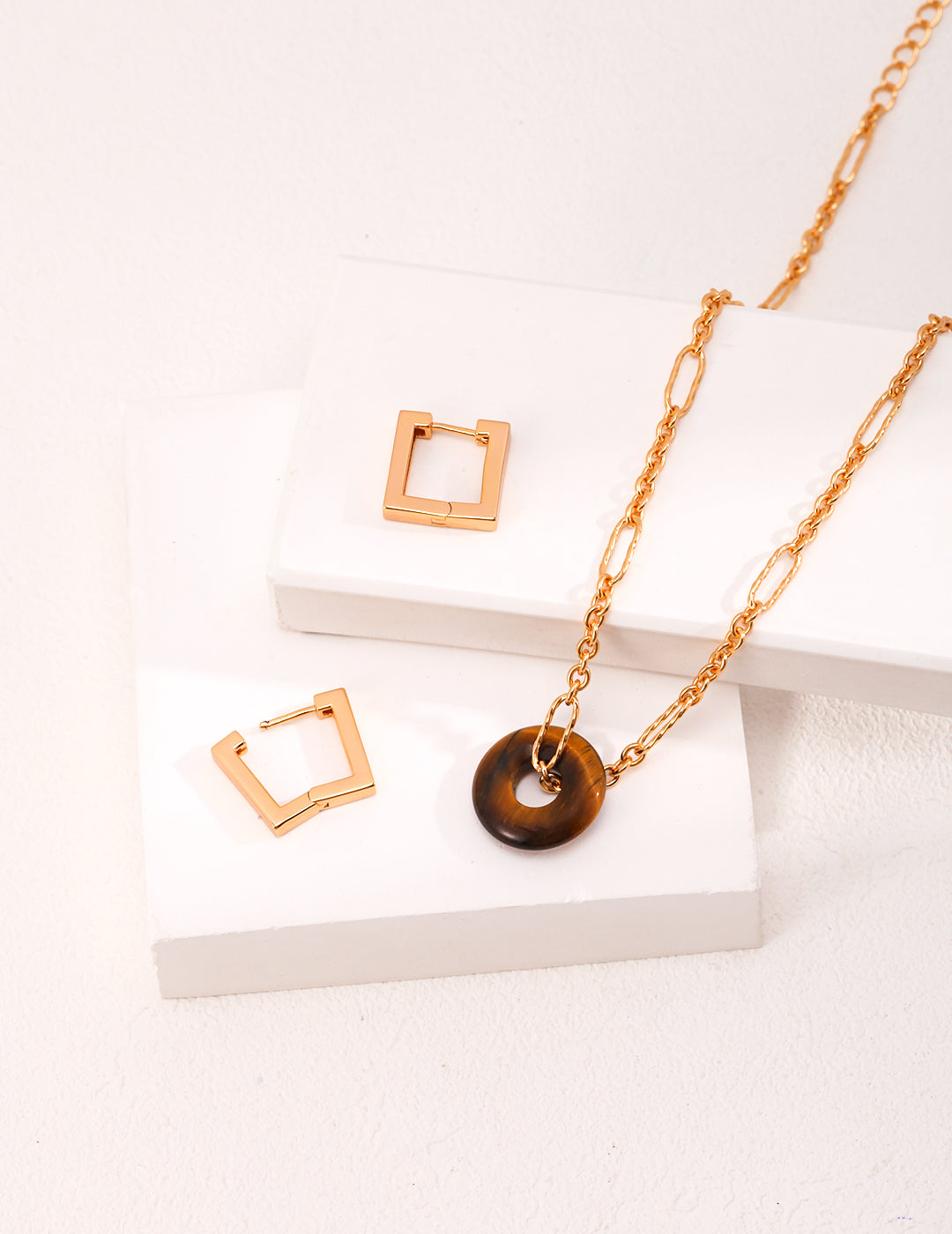 Gold jewelry set with tiger's eye stones on white surface.