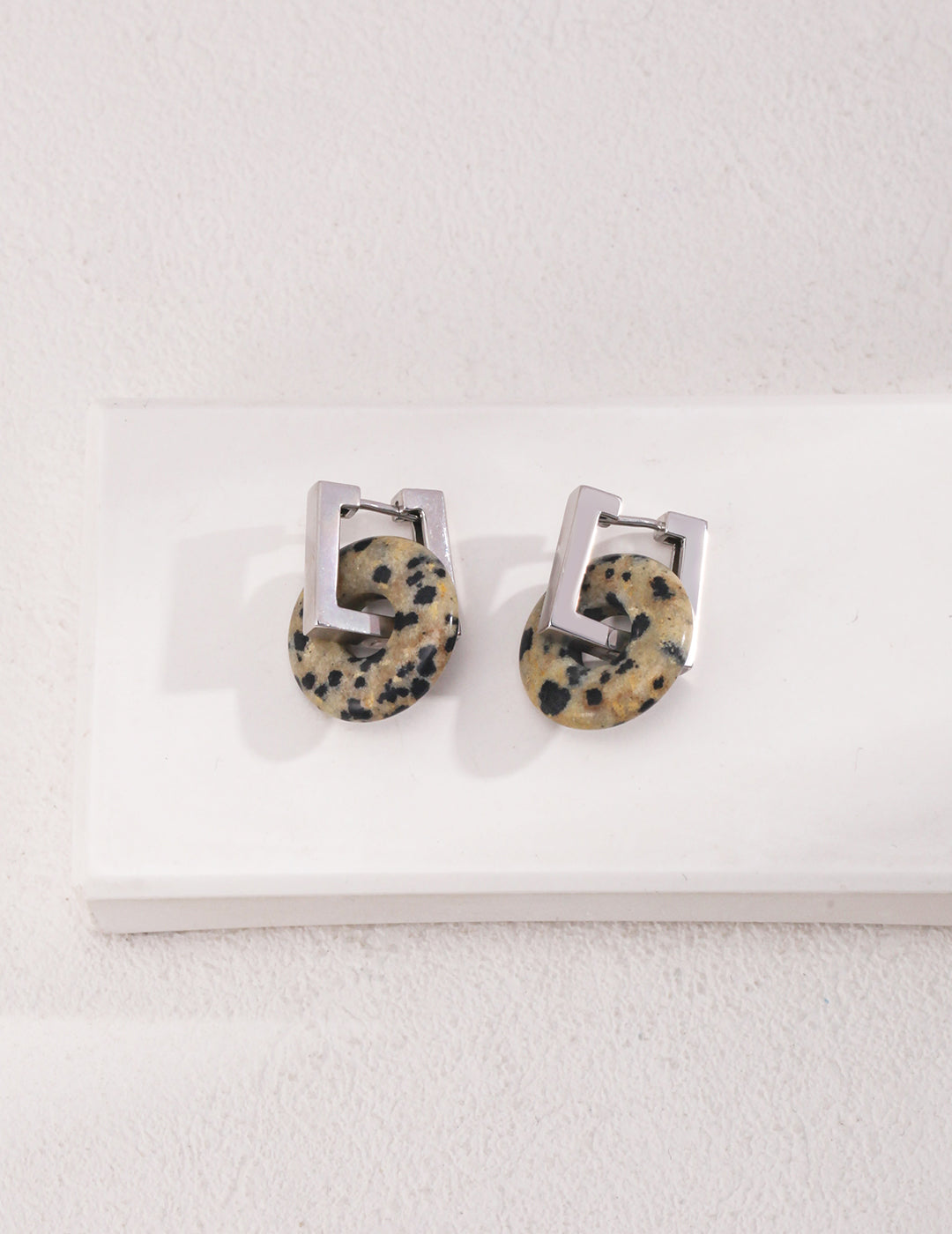 Stylish earrings featuring black and white design on gold square hoops with dalmatian jasper stones.