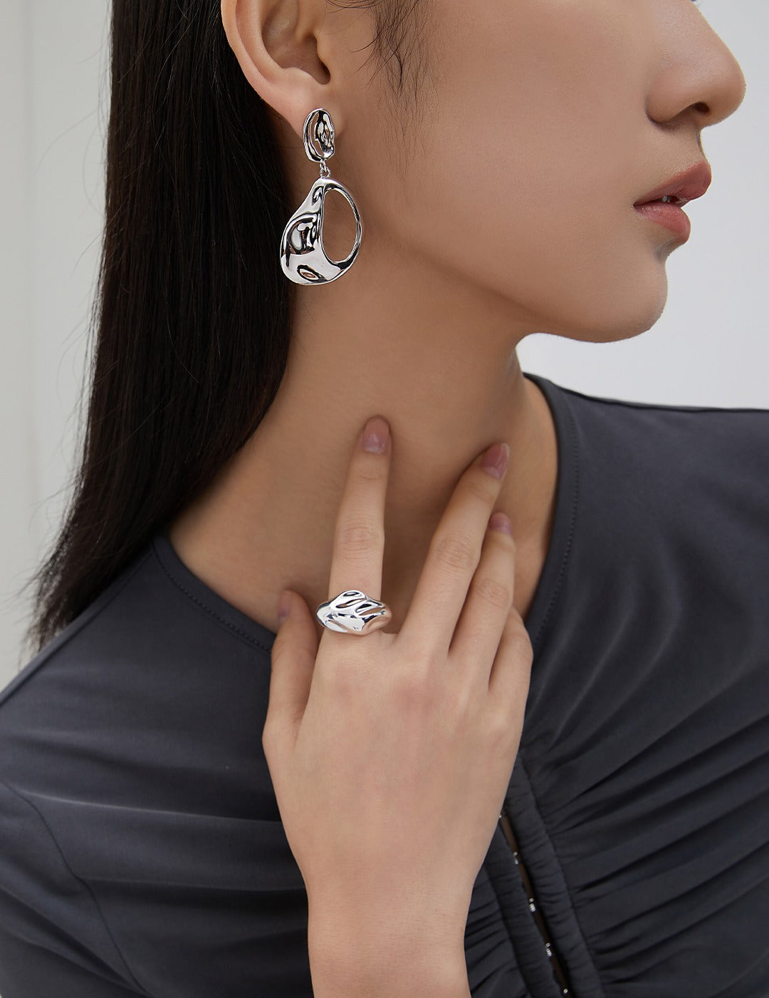 A woman wearing a silver satin motioned ring and matching earrings, adding elegance to her look.