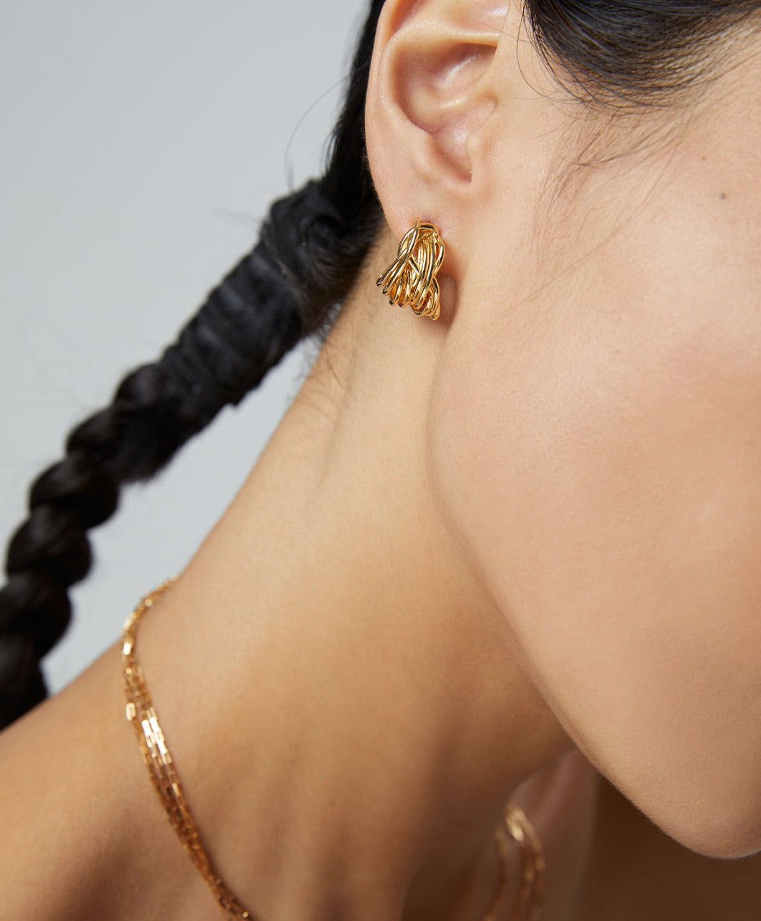 A woman adorned with a gold chain and a gold earring.