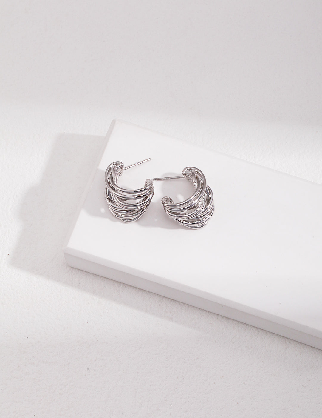 Stylish silver earrings resting on white surface.