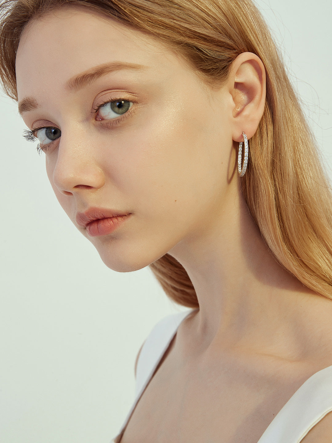 A stylish woman in a white top accessorized with sleek hoops earrings.