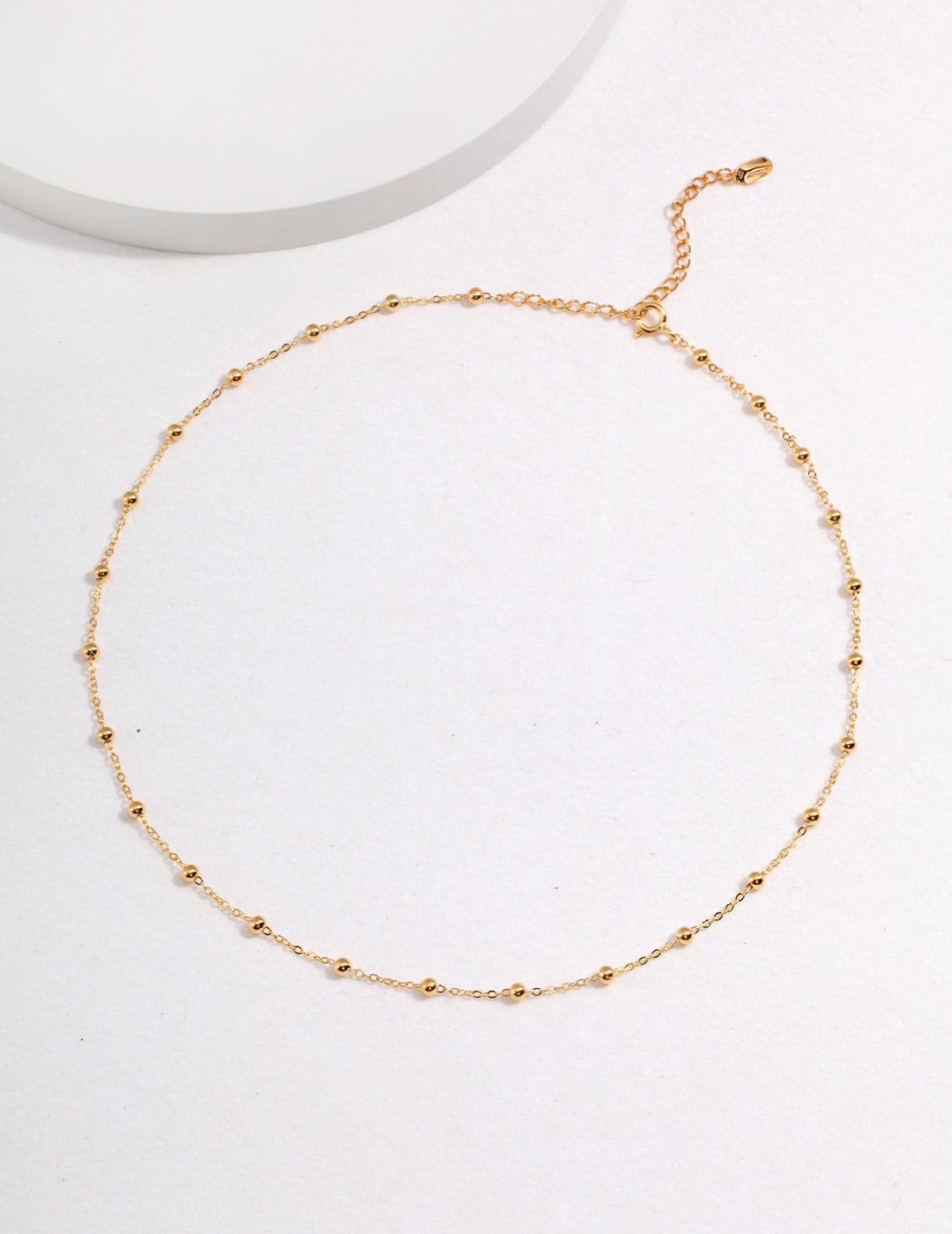 A gold chain necklace with beads interspersed, displayed on a white surface.