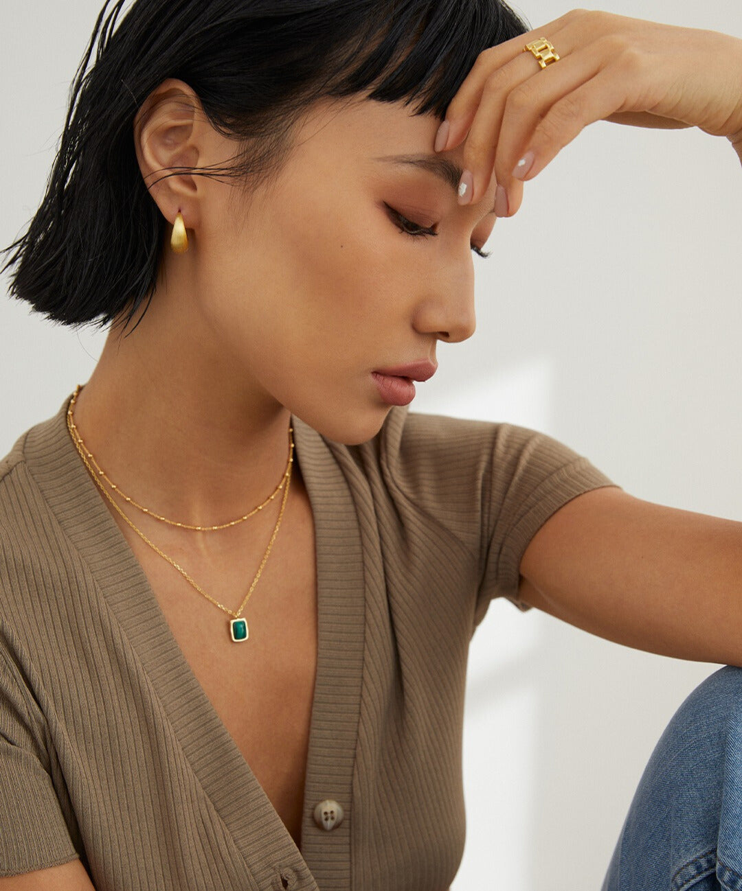 A woman in a brown shirt and gold jewelry, including a gold necklace with beads interspersed.