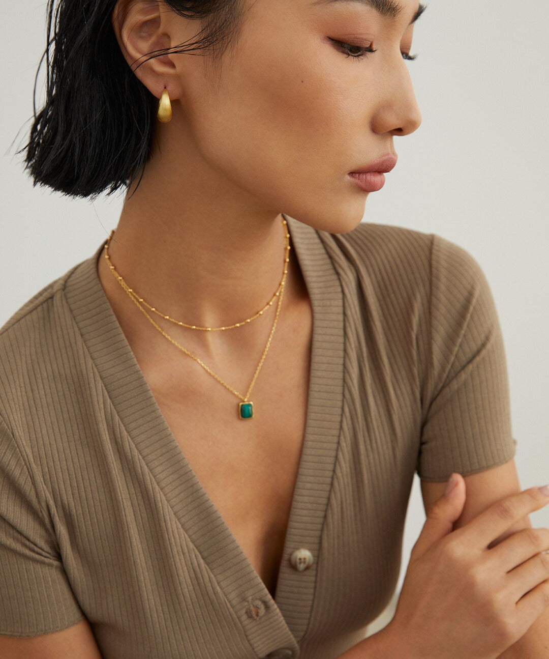 A model in a green necklace and gold earrings.